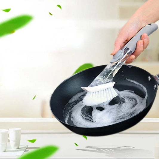 2-in-1 kitchen cleaning brush with a long handle, being used to scrub a frying pan with soap suds.